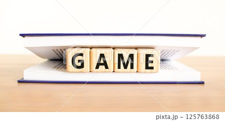 Game symbol. Concept word Game on beautiful wooden blocks in book. Beautiful wooden table white background. Business, lifestyle and game concept. Copy space. Game symbol. Concept word Game on beautiful wooden blocks in book. Beautiful wooden table white background. Business, lifestyle and game concept. Copy space. 125763868
