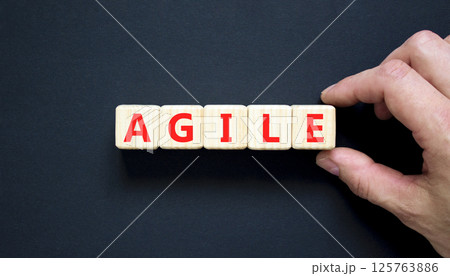Agile symbol. Concept word Agile on beautiful wooden blocks. Beautiful black table black background. Businessman hand. Business agile concept. Copy space. Agile symbol. Concept word Agile on beautiful wooden blocks. Beautiful black table black background. Businessman hand. Business agile concept. Copy space. 125763886