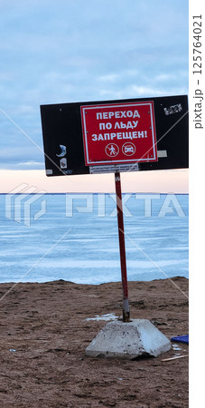 Winter landscape. Red warning sign Danger of going out on ice. Walking on melted snow on bay is dangerous. Vertical photo. High quality photo 125764021