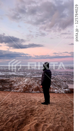 Spring landscape. Panoramic view of beautiful dawn on bay. Cumulus clouds over water in bright light. Ice, snow and rocks on coastline. Rising rays of sun are reflected in sea. Vertical photo. Spring landscape. Panoramic view of beautiful dawn on bay. Cumulus clouds over water in bright light. Ice, snow and rocks on coastline. Rising rays of sun are reflected in sea. Vertical photo. 125764029