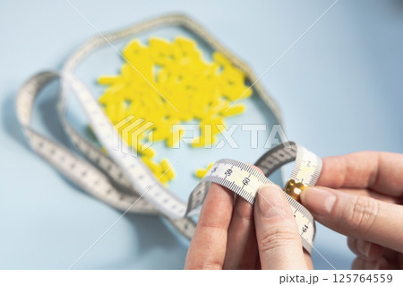 Female hands holding a measuring tape against pile of yellow pills 125764559