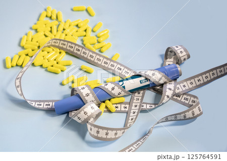 Ozempic syringe pen and measuring tape with a bunch of pills in the background 125764591