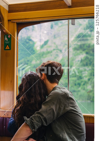 The couple sits close together in a train, gazing out at the lush green mountains. Their relaxed posture suggests they are enjoying the serene scenery during their journey. Konigsse Bavaria German The couple sits close together in a train, gazing out at the lush green mountains. Their relaxed posture suggests they are enjoying the serene scenery during their journey. Konigsse Bavaria German 125766218