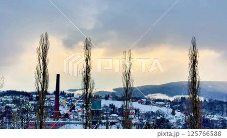 A serene winter landscape featuring trees set against a factory smoke stack in the distance A serene winter landscape featuring trees set against a factory smoke stack in the distance 125766588