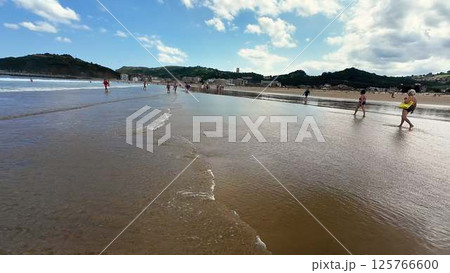 Enthusiastic Beach Walkers Relishing in the Joys of a Beautiful Sunny Day by the Calm Shoreline 125766600