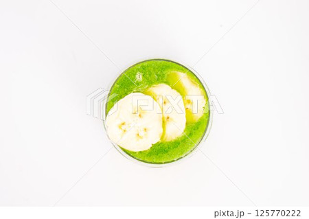 green smoothie with banana slices served in clear glass on white background healthy detox drink with tropical fruit topping. High quality photo green smoothie with banana slices served in clear glass on white background healthy detox drink with tropical fruit topping. High quality photo 125770222