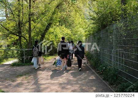 people walking outdoors through sunny park or open paved space during spring with trees and bright sky. High quality photo 125770224