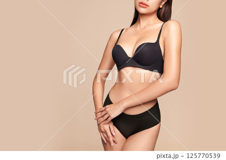 Confident beautiful young asian woman posing in black lingerie on beige background, Perfect body, 125770539
