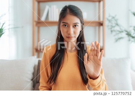 Young Asian woman with serious expression raising her hand stop gesture Young Asian woman with serious expression raising her hand stop gesture 125770752