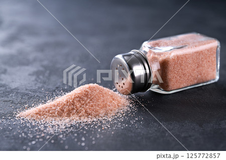 Spilled pink himalayan salt and salt shaker on on a black stone table, selective focus. 125772857