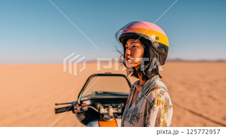 Portrait of young Japanese woman against sandy desert backdrop on motorbike journey, independence defined by woman's fearless energy and daring desert riding, copy space for active vacation concept Portrait of young Japanese woman against sandy desert backdrop on motorbike journey, independence defined by woman's fearless energy and daring desert riding, copy space for active vacation concept 125772957