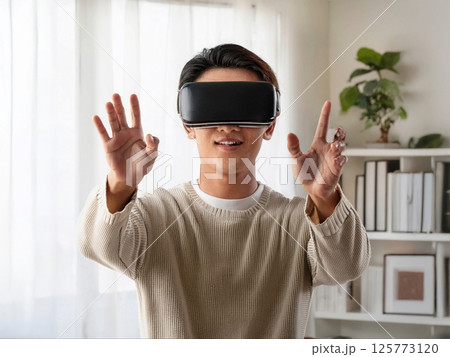 リビングでヘッドマウントディスプレイを付けて仮想現実を楽しむ男性 125773120
