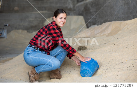 Woman pouring corn flour into bucket at animal feed warehouse Woman pouring corn flour into bucket at animal feed warehouse 125773297