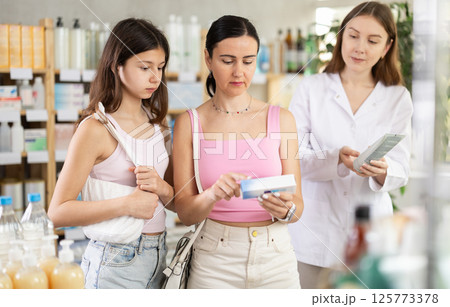 Woman with daughter choosing ointment with pharmacist Woman with daughter choosing ointment with pharmacist 125773378
