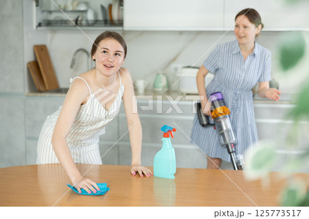 Adult daughter and mum veste tidy up the room - daughter dusts the table, mum vacuums room Adult daughter and mum veste tidy up the room - daughter dusts the table, mum vacuums room 125773517