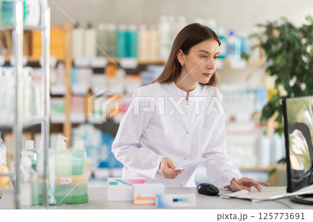 Young female pharmacist working with computer in chemist's shop Young female pharmacist working with computer in chemist's shop 125773691