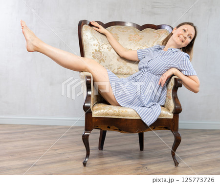 Girl settled down in vintage armchair with legs raised on armrest , put feet on handle of furniture 125773726