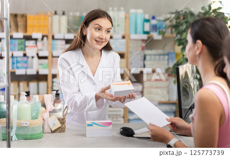 Portrait of woman pharmacist standing at prescription counter and helping mother and daughter choosing pill box and making decisions about pharmaceuticals and health care at pharmacy shop 125773739