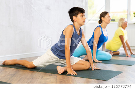 Mother, grandmother and teen son do exercise dove pose, Eka Pada Rajakapotasana. Mother, grandmother and teen son do exercise dove pose, Eka Pada Rajakapotasana. 125773774