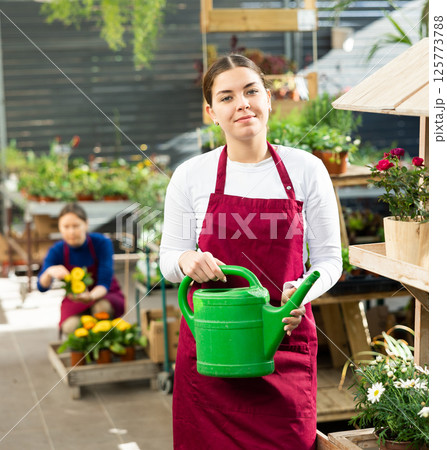 Gardener woman standing near various potted plants holding watering can in container garden Gardener woman standing near various potted plants holding watering can in container garden 125773788