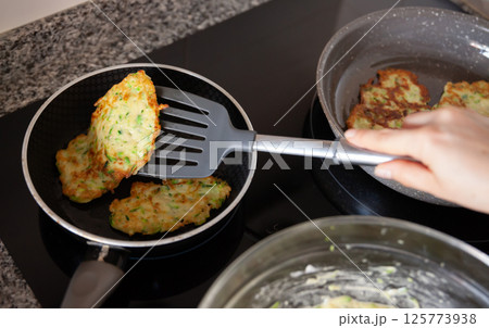 Process frying zucchini pancakes in frying pan in kitchen 125773938