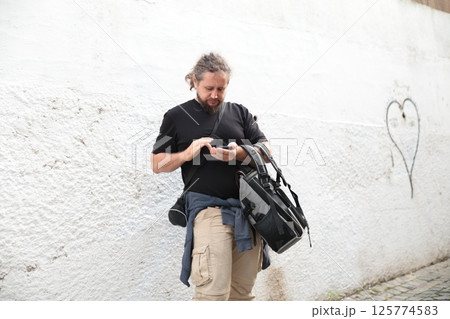 Photographer using smartphone app while leaning on white wall Photographer using smartphone app while leaning on white wall 125774583