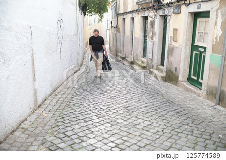 Tourist walking down cobblestone street in old european town with travel bag Tourist walking down cobblestone street in old european town with travel bag 125774589