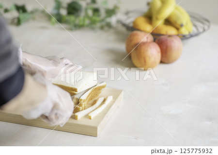 サンドイッチを切る女性の手、フルーツのある食卓 125775932