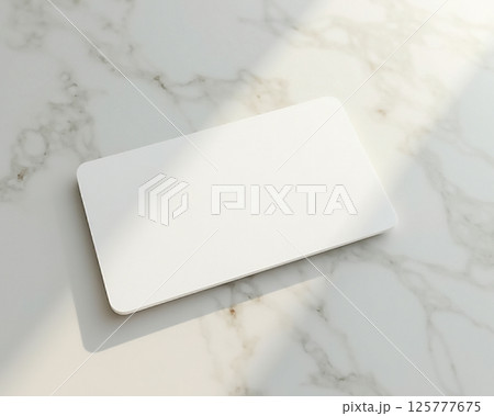 Flat white card placed on a marble surface with soft sunlight illuminating the scene during the day 125777675