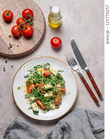 Healthy arugula salad with cherry tomatoes, mozzarella and pesto sauce on a light background Healthy arugula salad with cherry tomatoes, mozzarella and pesto sauce on a light background 125778257