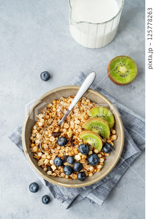 Homemade baked granola or muesli in a bowl with kiwi and blueberries on a light background Homemade baked granola or muesli in a bowl with kiwi and blueberries on a light background 125778263
