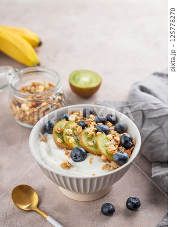 Natural greek yogurt with granola, kiwi and blueberries in a bowl on a light background Natural greek yogurt with granola, kiwi and blueberries in a bowl on a light background 125778270