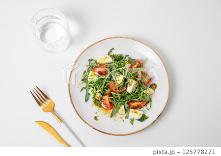 Fresh arugula salad with cherry tomatoes, mozzarella, pesto sauce on white background Fresh arugula salad with cherry tomatoes, mozzarella, pesto sauce on white background 125778271