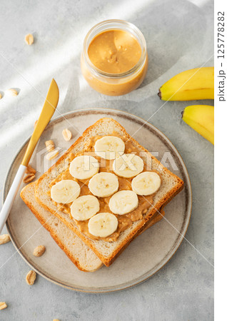 Peanut butter toast with banana on a plate on a light background with morning shadow. 125778282