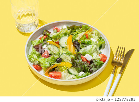 Vegetable salad with lettuce, olives and feta cheese on yellow background Vegetable salad with lettuce, olives and feta cheese on yellow background 125778293