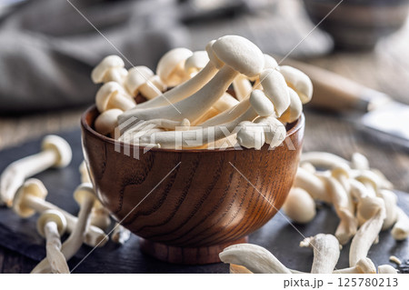 Raw white shimeji mushrooms in bowl on cutting board. 125780213