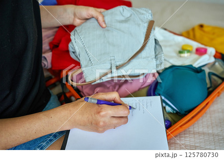 Woman writing travel checklist while packing suitcase 125780730