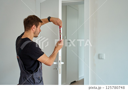 Man using spirit level to align door frame during installation 125780748