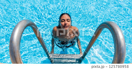 Beautiful woman in black swimsuit coming out of pool. Beautiful woman in black swimsuit coming out of pool. 125780958