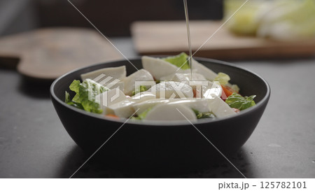 pour walnut oil onto salad with romaine lettuce, tomatoes and mozzarella in black bowl on concrete countertop pour walnut oil onto salad with romaine lettuce, tomatoes and mozzarella in black bowl on concrete countertop 125782101