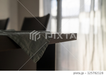 Dark green linen napkin on walnut table indoor with natural window light 125782128