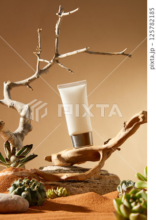 A cosmetic tube with a silver metal cap stood tilted on a brown tree trunk, with a rough rock underneath. The dry and leafless tree still grew, its top pointing to the sky, surrounded by succulents. A cosmetic tube with a silver metal cap stood tilted on a brown tree trunk, with a rough rock underneath. The dry and leafless tree still grew, its top pointing to the sky, surrounded by succulents. 125782185