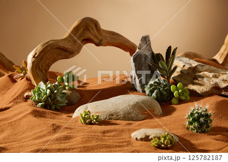 Desert objects such as boulders, rocks, logs, brown dead tree trunks and plants such as succulents and cacti are scattered around. Dry sand is blown by the wind to form undulating sand ripples. 125782187