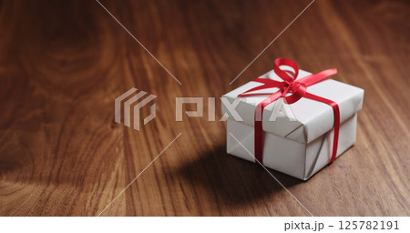 white gift box with red ribbon on walnut table 125782191