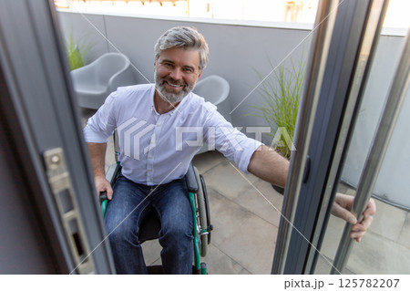 Gray-haired bearded mature man on a wheelchair opening the door to the office 125782207
