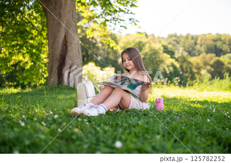 Young school girl enjoying her leisure time outside studying literature in nature Young school girl enjoying her leisure time outside studying literature in nature 125782252
