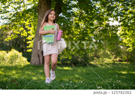 Child walking in park with backpack and bools in hands book on sunny day Child walking in park with backpack and bools in hands book on sunny day 125782262