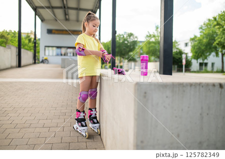 Little female skater adjusting protective gear on hands before skating Little female skater adjusting protective gear on hands before skating 125782349