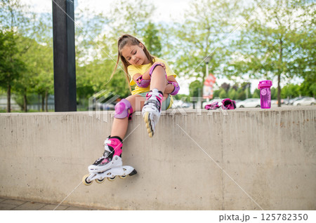 Child putting on knee pads getting ready for roller-blading Child putting on knee pads getting ready for roller-blading 125782350