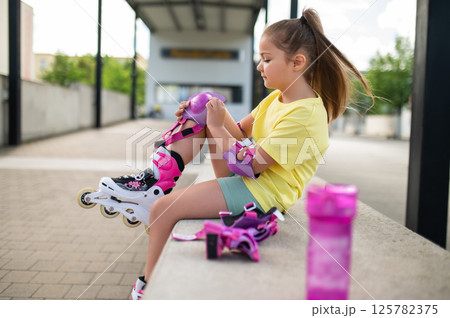 Little female skater adjusting protective gear on knees before skating Little female skater adjusting protective gear on knees before skating 125782375